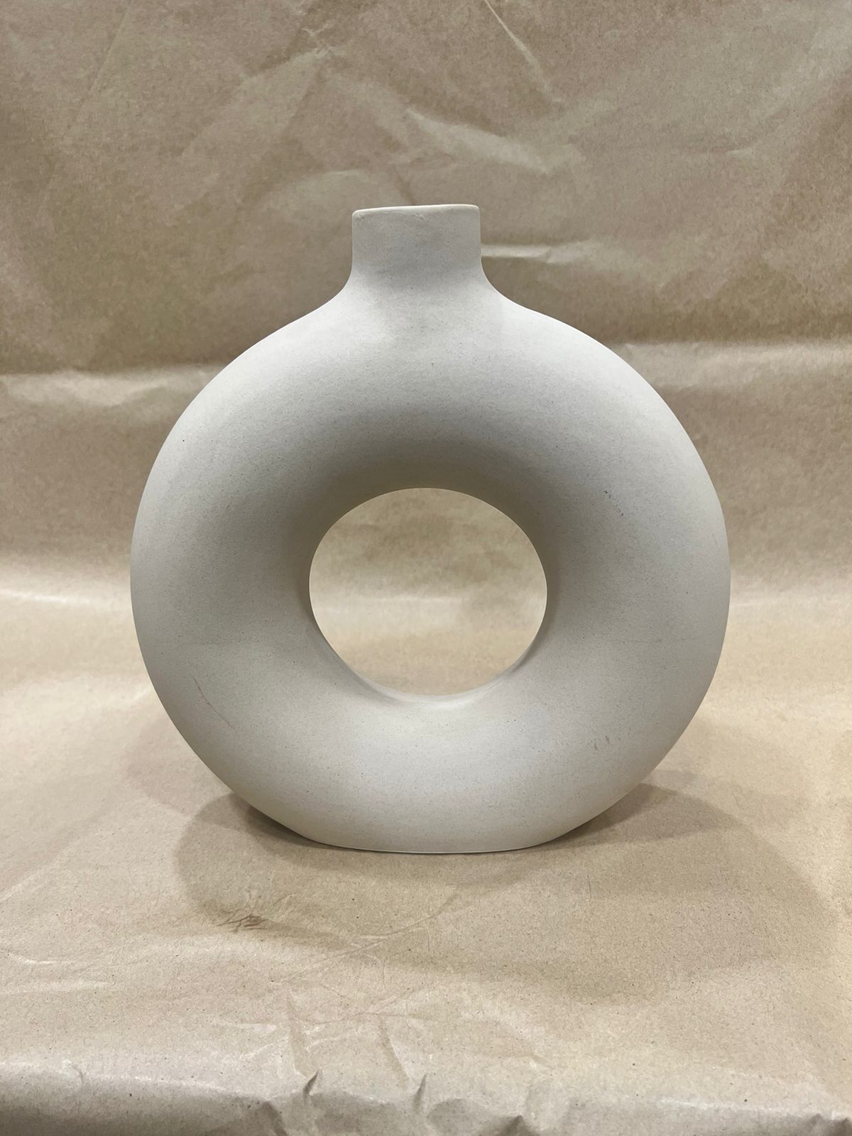 White ring-shaped ceramic vase on a neutral textured backdrop